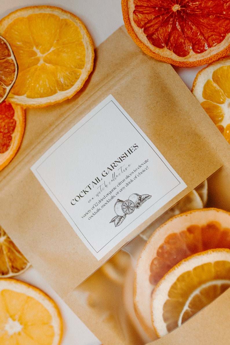 May include: A brown paper bag with a white label that reads "COCKTAIL GARNISHES sea witch collective variety of 12 dried organic citrus slices to elevate cocktails, mocktails, or any drink of choice!" The bag is filled with dried citrus slices in various colours, including orange, yellow, and red.