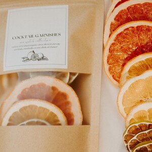 May include: A brown paper bag with a clear window showing dried citrus slices. The bag has a label that reads "Cocktail Garnishes as a whole collective" and "variety of 12 dried organic citrus slices to elevate cocktails, mocktails, or any drink of choice!"