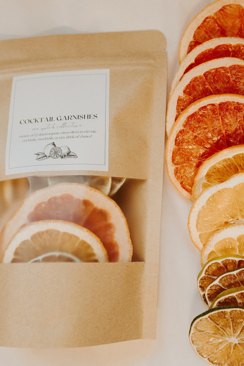 May include: A brown paper bag with a clear window showing dried citrus slices. The bag has a label that reads "Cocktail Garnishes as a whole collective" and "variety of 12 dried organic citrus slices to elevate cocktails, mocktails, or any drink of choice!"