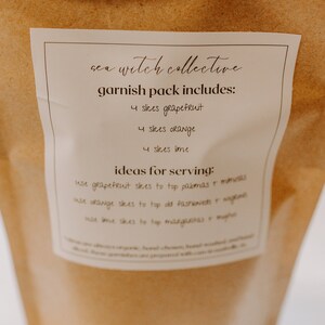 May include: A brown paper bag with a white label that says "sea witch collective garnish pack includes: 4 slices grapefruit 4 slices orange 4 slices lime ideas for serving: use grapefruit slices to top palomas & mimosas use orange slices to top old fashioneds & negronis use lime slices to top margaritas & mojitos"
