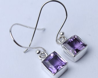 May include: A pair of silver earrings with square, purple amethyst stones. The earrings have a hook design for pierced ears. The amethyst stones are set in a silver bezel setting.
