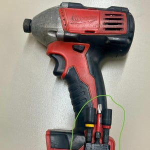 May include: A red and black cordless impact driver with a silver head. The tool has a black handle and a red base. Three drill bits are attached to the base, with yellow and red accents.