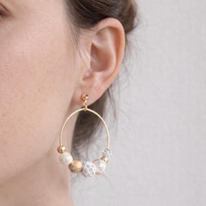 May include: Gold hoop earrings with a cluster of white, gold, and clear beads. The earrings are circular and hang from a small gold post. The beads have a variety of textures and sizes, adding visual interest to the jewelry.