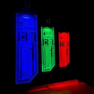 K&ouml;nnte beinhalten: Drei leuchtende rechteckige Tafeln in Blau, Gr&uuml;n und Rot, jeweils mit dem Text "AE-1701". Die Tafeln haben ein Leiterplattendesign und sind vor einem schwarzen Hintergrund aufgeh&auml;ngt, was eine futuristische &Auml;sthetik erzeugt.