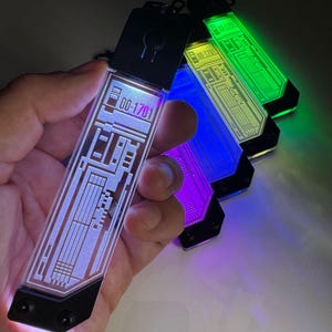 K&ouml;nnte beinhalten: Eine Sammlung leuchtender Schl&uuml;sselanh&auml;nger in verschiedenen Farben, darunter Blau, Lila und Gr&uuml;n. Jeder Schl&uuml;sselanh&auml;nger hat ein rechteckiges Design mit ge&auml;tzten Mustern und der Nummer "00-1701". Die Schl&uuml;sselanh&auml;nger haben eine schwarze Oberseite mit einem Schl&uuml;sselloch-Design.