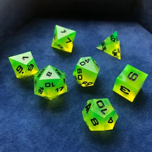May include: A set of seven polyhedral dice featuring a vibrant neon yellow and green gradient finish with bold black numerals. The collection includes various geometric shapes such as a d20, d12, d10, d8, d6, and d4, all displaying clear, legible digits.