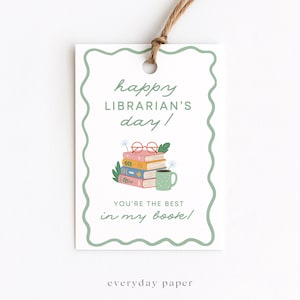 May include: A white gift tag with a green scalloped border and a string. The tag reads "happy LIBRARIAN'S day!" with an illustration of books, glasses, and a mug. The text "YOU'RE THE BEST in my book!" is also present.