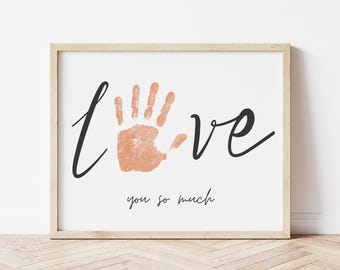 May include: A framed print with a handprint in the center and the word "love" written in cursive. The text "you so much" is written below the handprint.