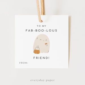 May include: A white Halloween gift tag with a tan leather string. The tag features a friendly ghost illustration holding a pumpkin bucket. Text reads "TO MY FAB-BOO-LOUS FRIEND!" and "FROM:" with "everyday paper" at the bottom.