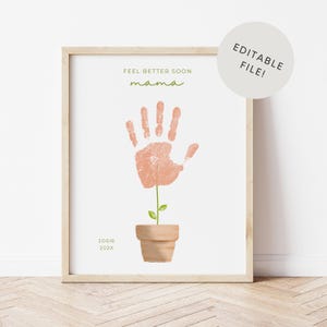 May include: A framed print with a light wood frame. The print features a handprint in the shape of a flower, with the words "Feel Better Soon mama" in green script. The bottom of the print reads "JOSIE 202X". A white circle with the words "EDITABLE FILE!" is in the upper right corner.