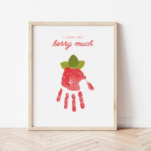 Könnte beinhalten: Ein druckbarer Kunstdruck mit einem roten Handabdruck in Form einer Erdbeere mit grünen Blättern. Der Text "I love you berry much" ist in Rosa über der Erdbeere geschrieben.