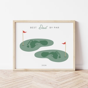 May include: Framed print with a light wood frame. The print features two green golf course greens with footprints, red flags, and the text "BEST Dad BY PAR" above the greens. The year "2026" is printed below the greens.