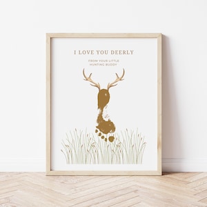 Peut inclure: Impression encadrée avec un motif d'empreinte de cerf. L'œuvre présente une silhouette de cerf créée à partir d'une empreinte de pied, avec des bois et le texte "I LOVE YOU DEERLY FROM YOUR LITTLE HUNTING BUDDY" en marron sur fond blanc.