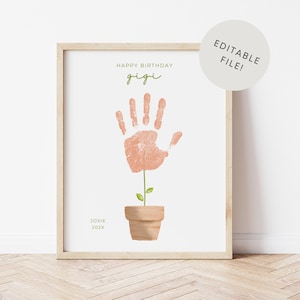 May include: A framed print with a handprint design. The handprint is peach-colored and resembles a flower growing from a terracotta pot. The text reads "Happy Birthday Gigi" and "Josie 202X". A circular sticker says "Editable File!"