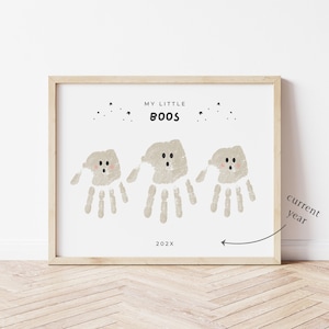 May include: A framed print with a light wood frame. The print features three ghost figures made from handprints, with the text "MY LITTLE BOOS" and the year "202X". The ghosts are light beige with black eyes and a pink blush.