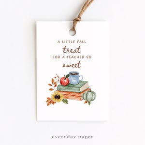 Puede incluir: Una etiqueta de regalo rectangular blanca con cordel marrón, que presenta el texto A LITTLE FALL treat FOR A TEACHER SO sweet. Debajo del texto hay una ilustración en acuarela de dos libros apilados, una manzana roja, una taza azul, un girasol y una calabaza verde.
