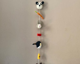 Puede incluir: Un móvil de animales de fieltro con un panda, un conejo, un pingüino, un oso y una zanahoria colgando de una cuerda blanca. El móvil está colgado del techo.