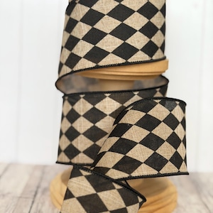 May include: A roll of wired ribbon featuring a repeating black and tan diamond pattern. The fabric has a visible woven texture, and the edges of the ribbon are finished with a thin black stitched border, creating a structured look for the material.