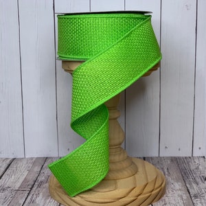 May include: A roll of bright green burlap ribbon with a woven texture. The ribbon is displayed on a wooden spool.