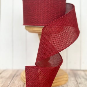 May include: A spool of red burlap ribbon with a textured weave. The ribbon is displayed on a wooden spool stand.