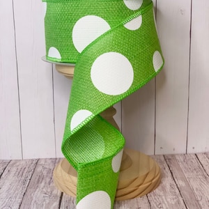 May include: Green and white polka dot ribbon with a burlap texture. The ribbon is rolled up on a wooden spool.