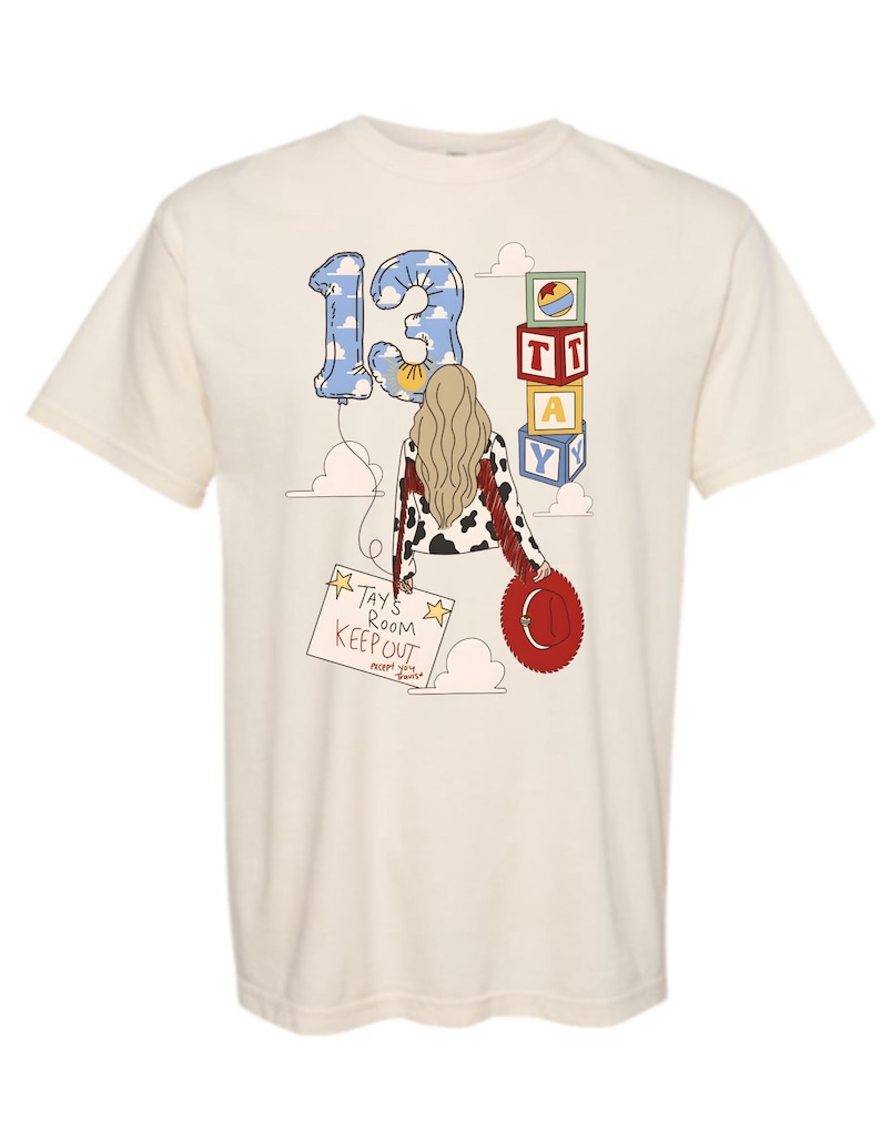 Puede incluir: Una camiseta color crema con un gr&aacute;fico de una persona de cabello rubio largo que viste una chaqueta con estampado de vaca y flecos rojos. El dise&ntilde;o incluye un globo azul con nubes en forma de n&uacute;mero 13, bloques de letras, un sombrero de vaquero rojo y un letrero que dice TAY'S ROOM KEEP OUT except you Travis.