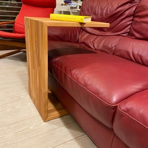 Può includere: Un tavolino da salotto in legno con un piano rettangolare e un design curvo e aperto. Il tavolino è accanto a un divano in pelle rossa e ha un libro giallo sopra.