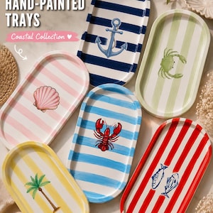 May include: Six oval-shaped trays featuring hand-painted designs including a blue anchor, a green crab, a pink seashell, a red lobster, a yellow palm tree, and two blue fish. Each tray displays vertical or horizontal stripes in various colors.