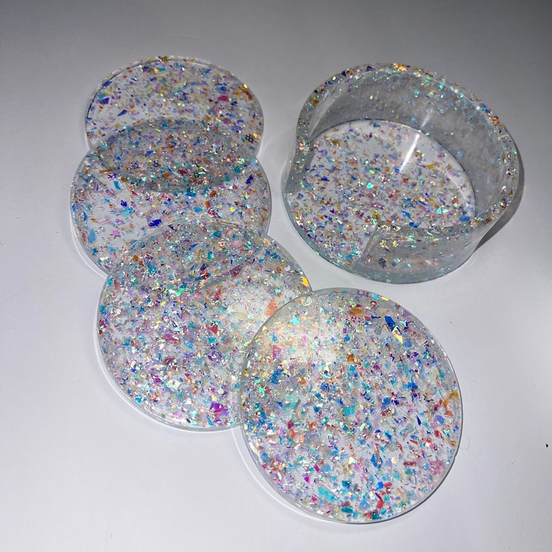 Op de afbeelding: Set van vijf ronde onderzetters van heldere hars en een houder. Elke onderzetter en de houder zijn ingebed met iriserende, kleurrijke glitterstukjes. De houder is gebogen.