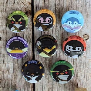 May include: A collection of nine round pinback buttons featuring cartoon penguins in various fantasy class roles. Each button has a different color scheme and text label, including "Druid," "Bard," "Wizard," "Dungeon Master," "Barbarian," "Fighter," "Rogue," and "Ranger."