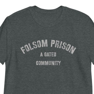 May include: A dark heather grey t-shirt with a white distressed graphic that reads "Folsom Prison A Gated Community".