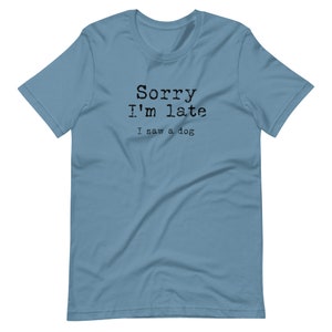 May include: A light blue t-shirt with the text "Sorry I'm late I saw a dog" printed in black.