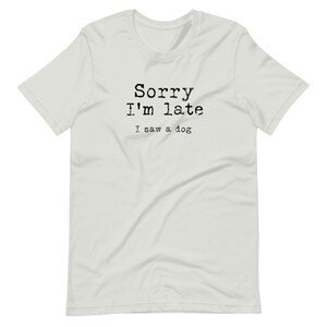 May include: White t-shirt with black text that reads "Sorry I'm late I saw a dog."