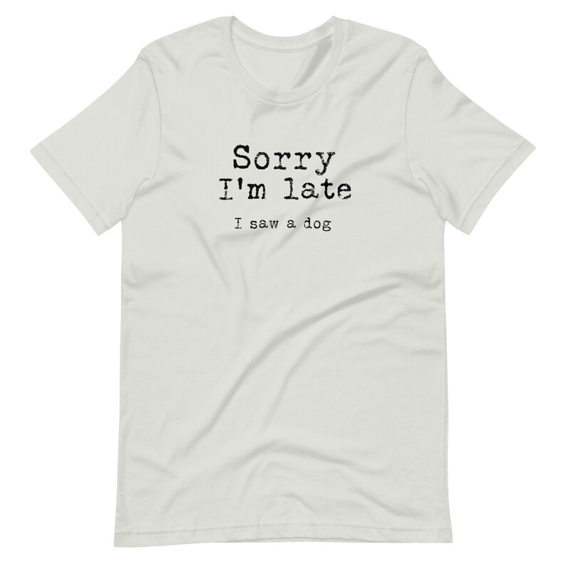 May include: White t-shirt with black text that reads "Sorry I'm late I saw a dog."