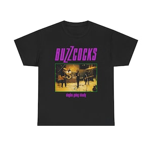 May include: Black t-shirt featuring the band name "Buzzcocks" in purple block letters above a rectangular image of the band performing live. Below the image, the text reads "singles going steady".