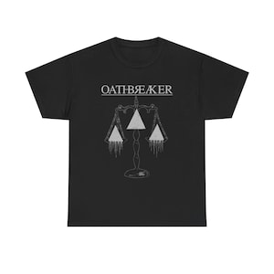 Peut inclure: T-shirt noir avec le mot "OATHBREAKER" au-dessus d'un dessin de balance. La balance a trois poids triangulaires avec des lignes dégoulinantes, créant une esthétique gothique.