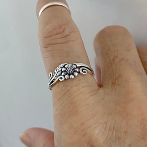 Puede incluir: Un anillo de plata con un diseño floral que presenta un girasol y hojas.