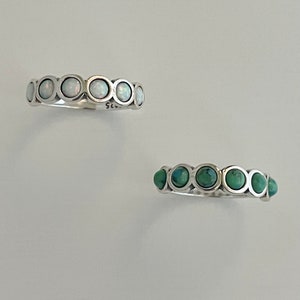 Op de afbeelding: Twee zilveren ringen met een rij ronde stenen. De bovenste ring heeft witte opaalstenen. De onderste ring heeft turquoise stenen.