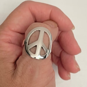 May include: A silver peace sign ring. The ring is worn on a person's thumb.