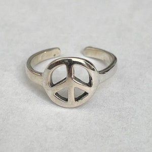 May include: Silver peace sign toe ring. The ring is adjustable and features a simple peace sign design.