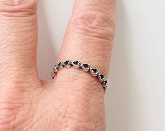 May include: A silver ring with a row of small black heart-shaped stones.