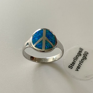 May include: A silver ring with a blue opal peace sign. The ring is on a white surface with a sticker that says "Sterling silver verring 900".