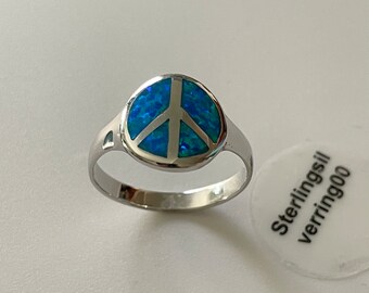 Puede incluir: Un anillo de plata con un símbolo de paz de ópalo azul. El anillo está sobre una superficie blanca con una etiqueta que dice "Sterling silver verring 900".