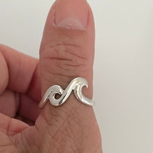 Op de afbeelding: Een zilveren golfring gedragen op de duim. De ring is simpel van ontwerp met een enkele golfvorm.
