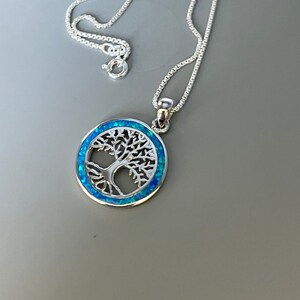 May include: A silver necklace with a blue opal tree of life pendant. The pendant is round and features a detailed tree design.