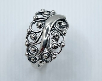 May include: A silver ring with a delicate, intricate design featuring a swirling pattern of small circles and a smooth, curved band.