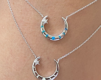 Puede incluir: Dos collares de plata con colgantes de luna creciente. El colgante superior tiene detalles de ópalo azul y el colgante inferior tiene detalles de ópalo blanco. Ambos colgantes tienen una pequeña estrella en la parte superior.
