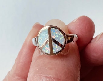 May include: A silver ring with a white opal peace sign.