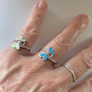 May include: Two silver rings with dragonfly designs. One ring features a blue opal dragonfly, and the other ring features a green opal dragonfly.