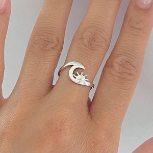 May include: A silver ring with a crescent moon design and a sun inside the moon.